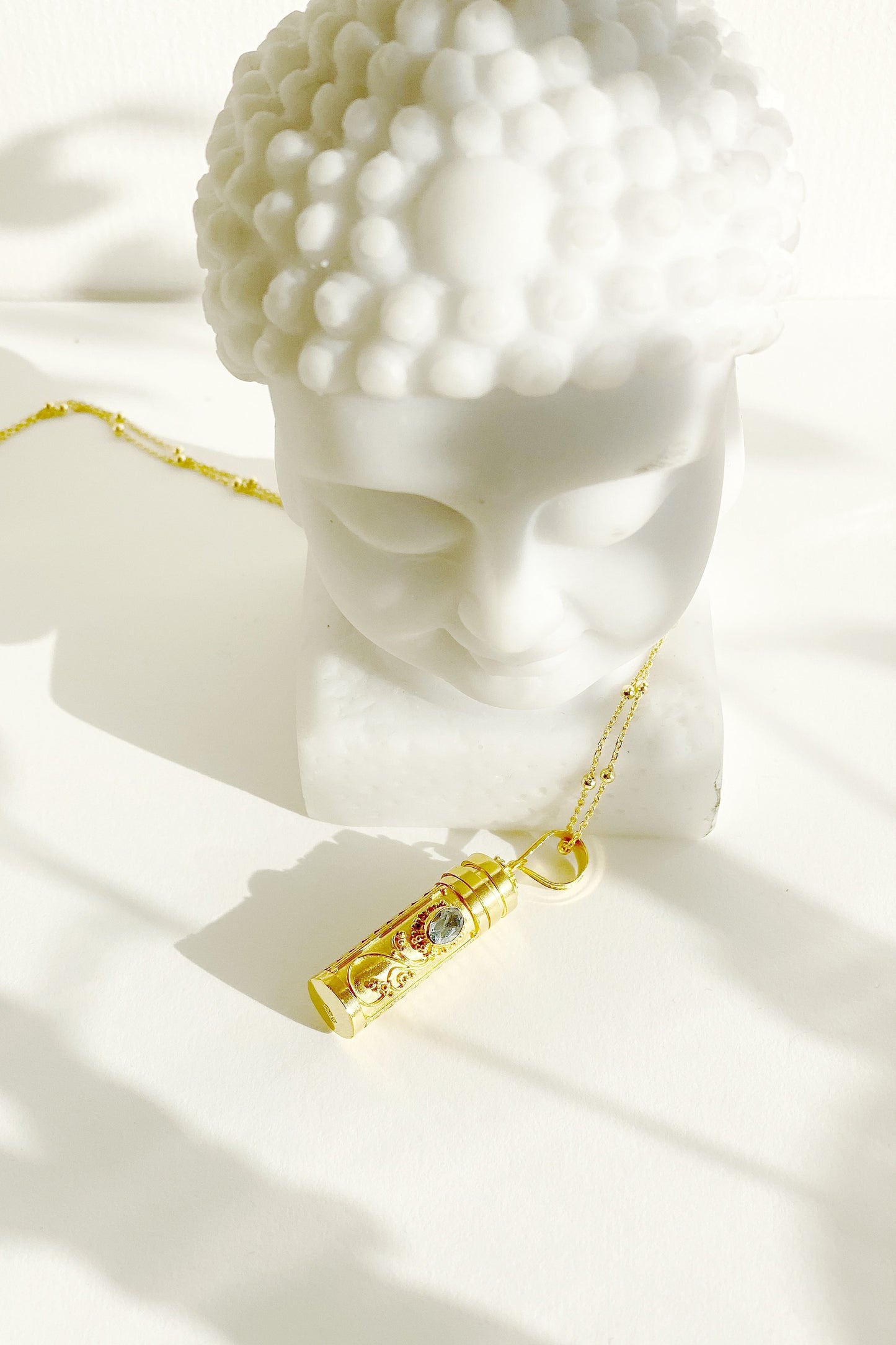 Blue Topaz Wishing Locket on a surface with its chain draped over the base of a bust