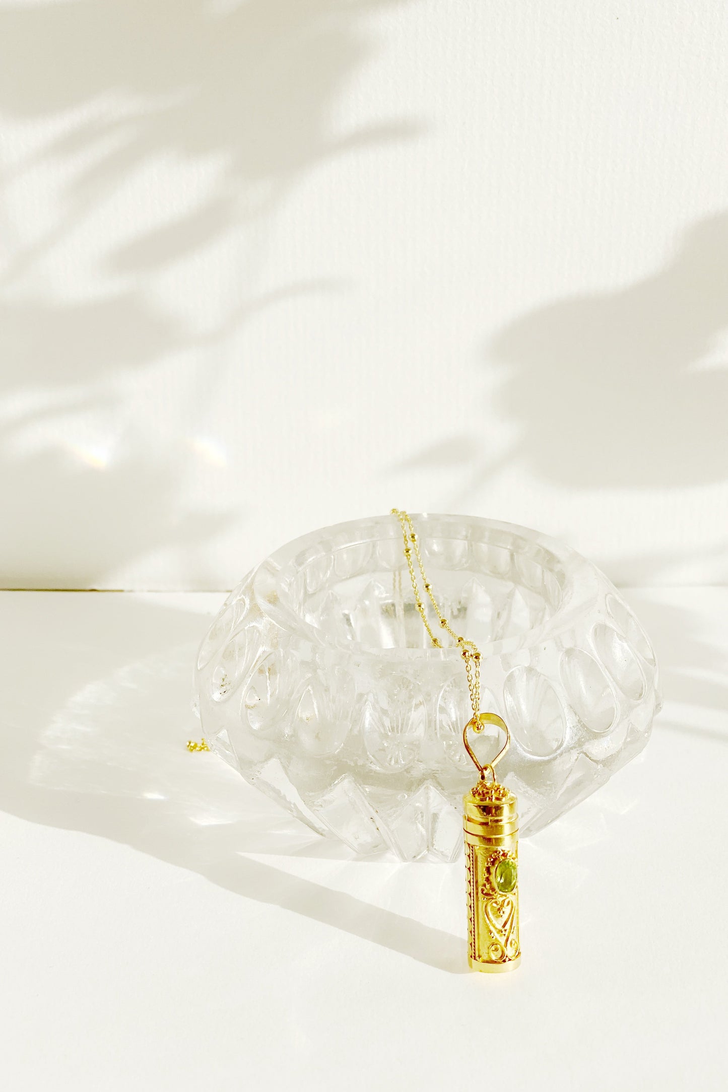 Peridot Wishing Locket with chain draped over glass vessel